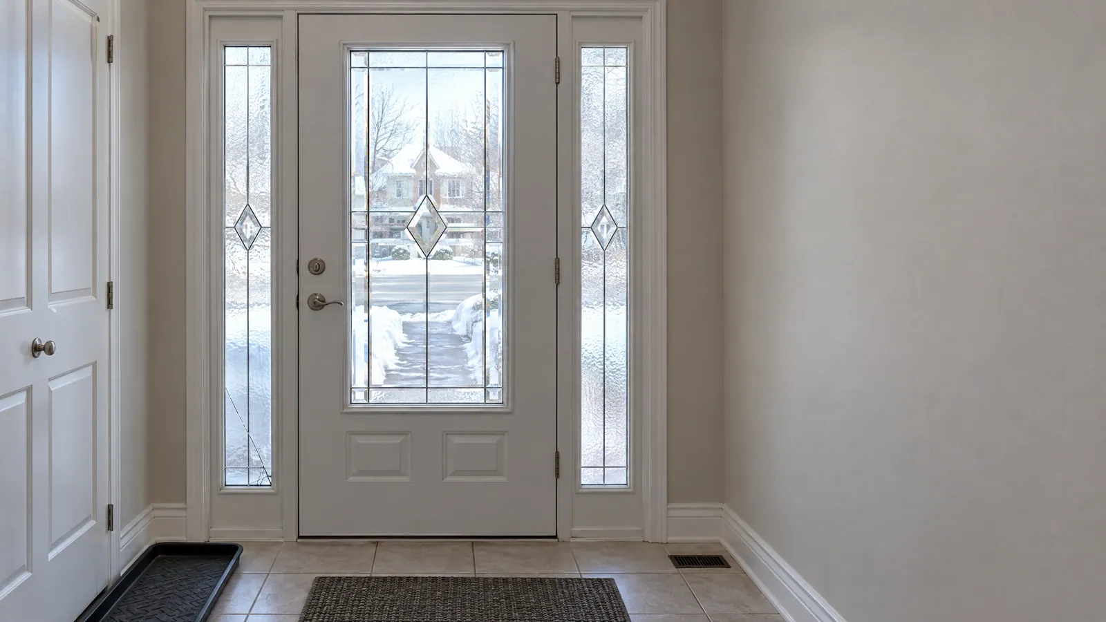 Front hall with a white door holding a bevelled, leaded-look glass insert between two textured sidelights, a thin crack low in the left sidelight, snow outside