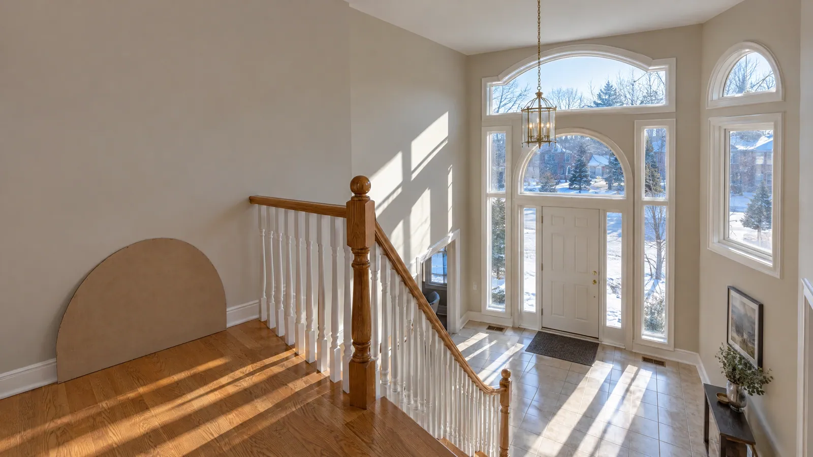Two-storey foyer with tall windows under an eyebrow arch and a half-round, and a cardboard arch template leaning on the landing